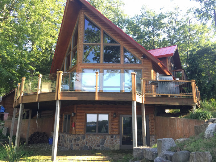 A large log home with glass windows and a red roof.